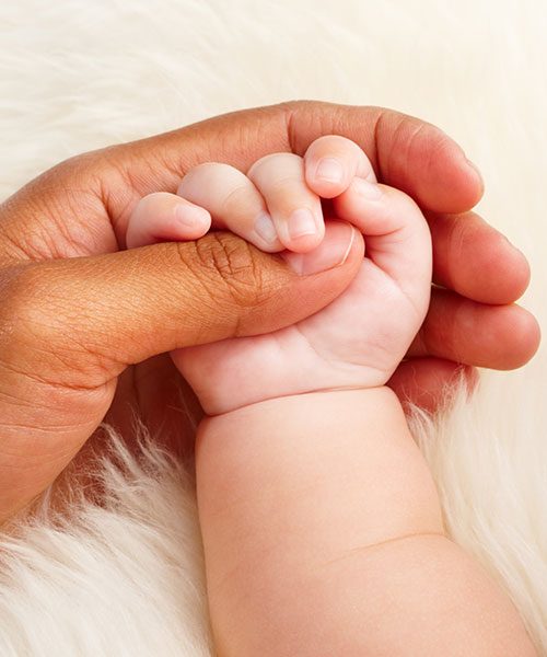 mains de bébé serrant le pouce d'une main d'adulte