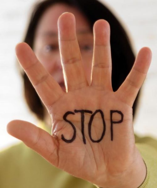 Femme tendant la paume de sa main sur laquelle est écrit "Stop"