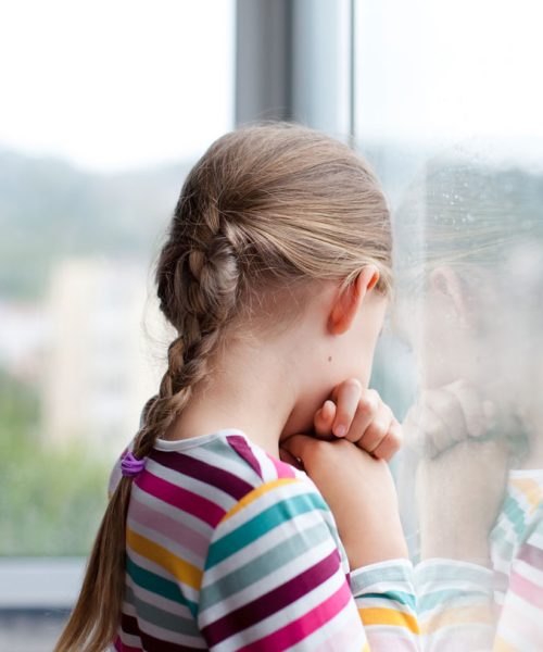 Petite fille triste devant une fenêtre